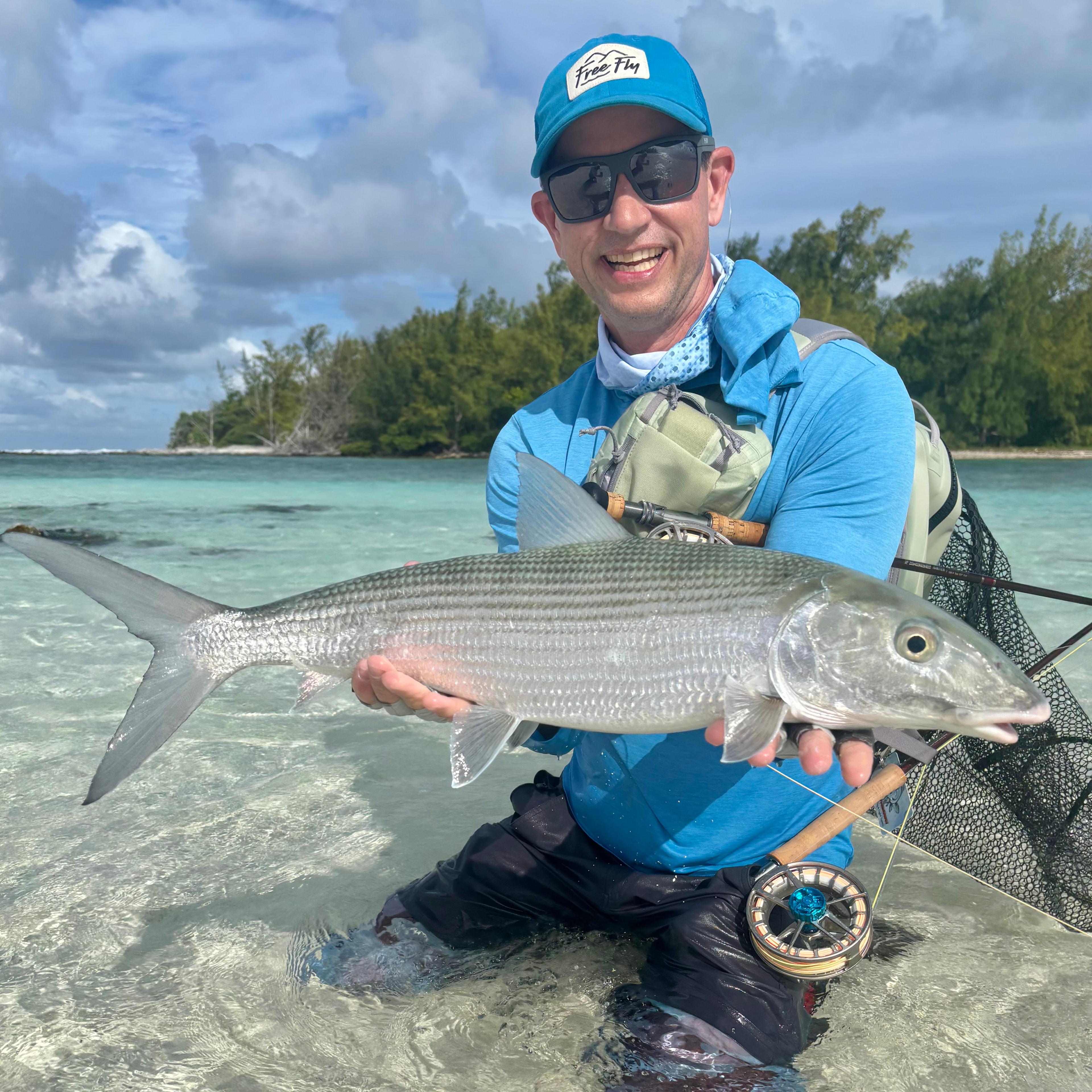 Bonefish on fly in French Polynesia — angler kneeling in crystal-clear tropical shallows holding a trophy bonefish